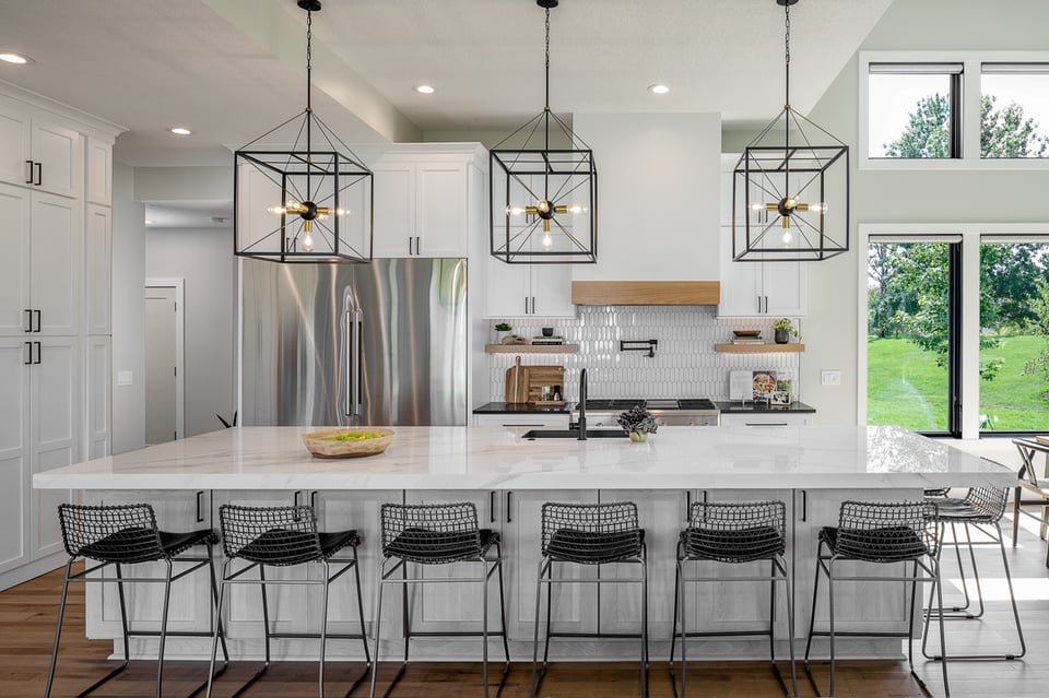 A Des Moines, IA, kitchen remodel project, featuring white cabinetry, white tile backsplash, and black metal accents. Image by Compelling Homes