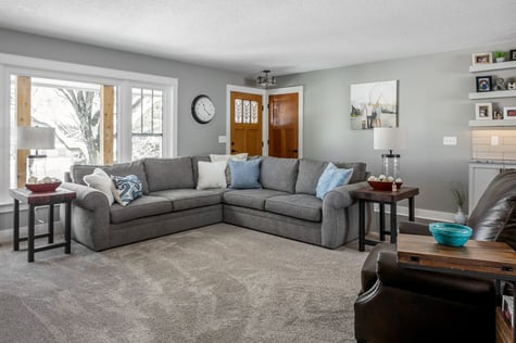 Whole Home Remodel Living Room with Floating Shelves Large Windows and Comfortable Sectional Couch | Compelling Homes