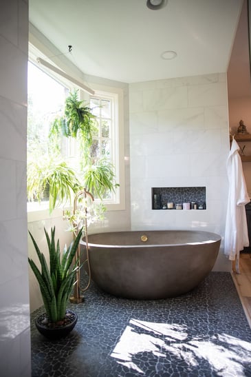 Freestanding tub with plants and freestanding mixer tap and pebble floor with uplighting