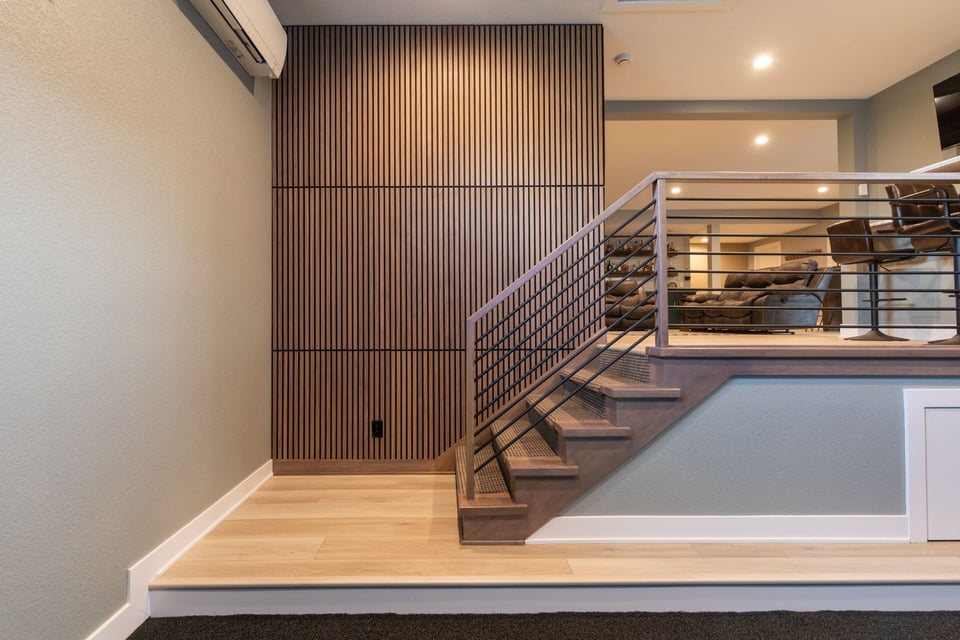 Wooden staircase connecting the upper deck of a home to the lower. A door leading to the basement visible