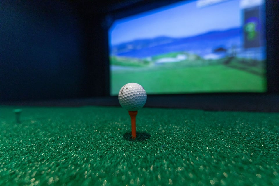 A gulf ball on a tee pinned into an artificial turf in a room designed for game stimulation