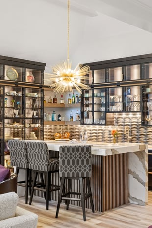 Modern wet bar with sputnik chandelier, glass-front cabinets, marble waterfall island, and mid-century barstools