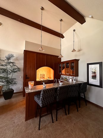 Traditional wet bar with cherry cabinets, arched alcove with niche lighting, and patterned upholstered stools before remodel