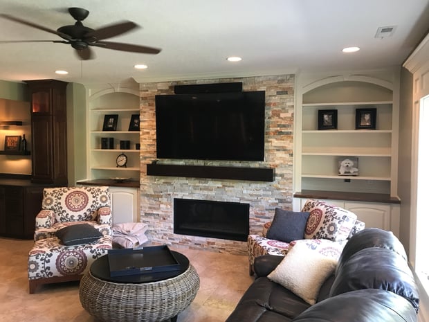 Updated basement living room with stacked stone fireplace surround, white built-in shelving, and mounted TV