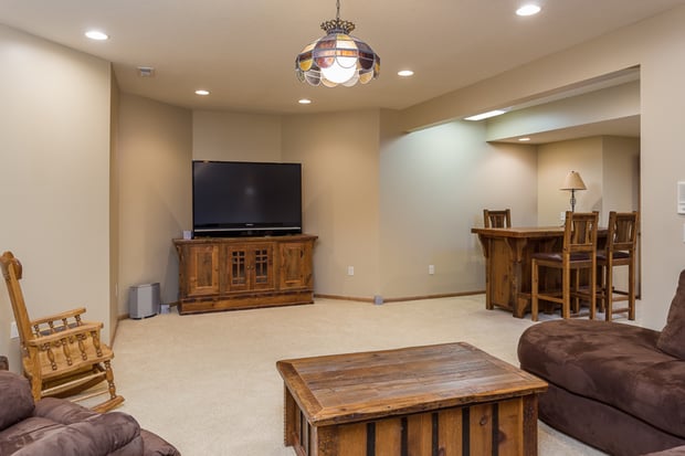 Traditional basement living room with dated stained-glass pendant, brown sofas, and beige carpet before remodel