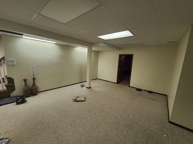 Empty unfinished basement with drop ceiling, fluorescent lights, and beige carpet before remodel