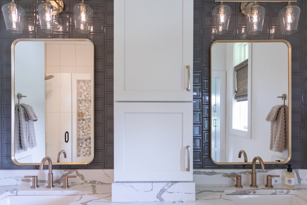 Modern bathroom with rounded brass-framed mirrors, dark tiled walls, marble waterfall counters, and brass fixtures