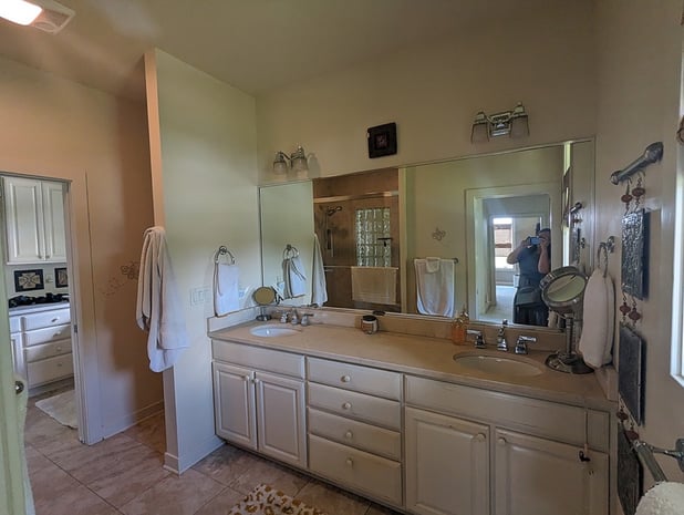 Outdated primary bathroom with double white cabinets, beige walls, dated lighting, and white tile floor before remodel