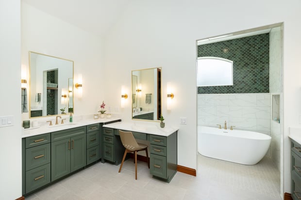 Modern primary bathroom with sage green cabinets, herringbone tile shower, freestanding tub, and brass-framed mirrors