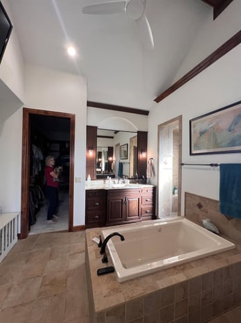Traditional primary bathroom with cherry wood vanity, vaulted ceiling, granite counters, and tiled soaker tub before remodel