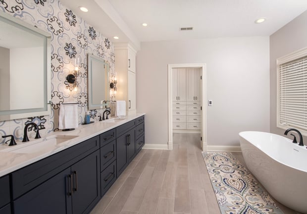Modern bathroom with navy vanity, ornate Moroccan tile backsplash, freestanding tub, and gold-framed mirrors