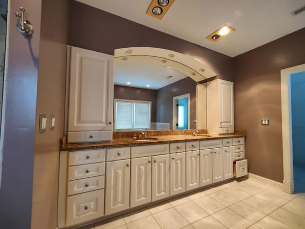 Outdated bathroom with arched mirror inset, white raised-panel cabinets, brown granite, and beige tile floor before remodel