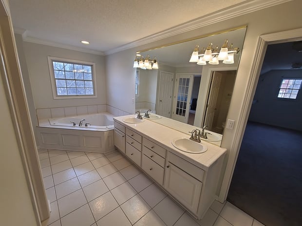 Outdated bathroom with double white cabinets, dated lighting, and corner jetted tub with tile surround before remodel