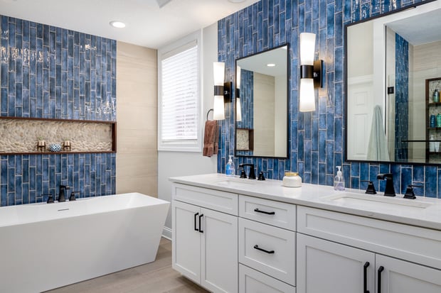 Modern bathroom with white shaker vanity, blue tile feature wall, freestanding tub, and pebble-accent niche