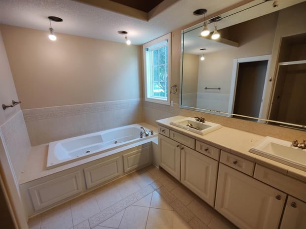 Dated bathroom with oak vanity cabinets, cream tile floors, and jet tub with tile surround before remodel