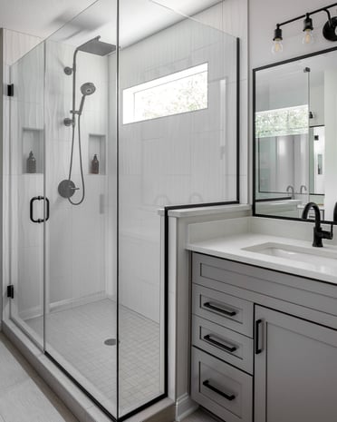 Modern industrial bathroom with white wave-tile shower, gray vanity, and black-framed glass enclosure