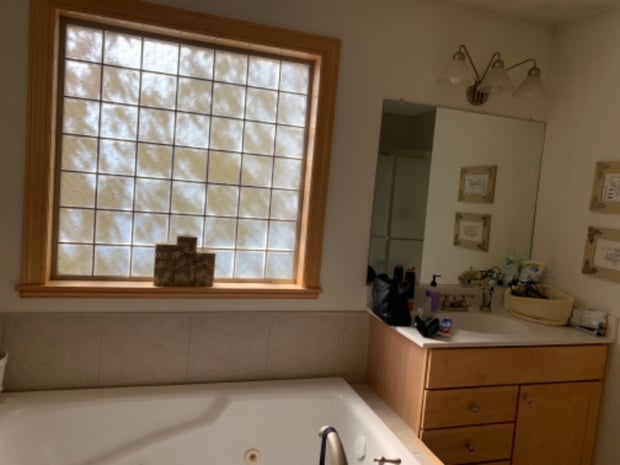 Outdated bathroom with maple vanity, glass block window, cream tile, and original jetted tub before remodel