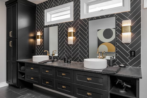 Dramatic bathroom with black herringbone feature wall, dark vanity with brass hardware, and brass sconces