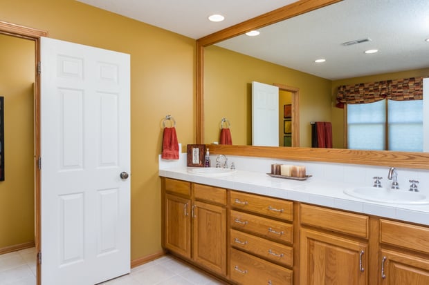 Dated bathroom with oak vanity, oak-framed mirror, white tile counter, and mustard walls before remodel