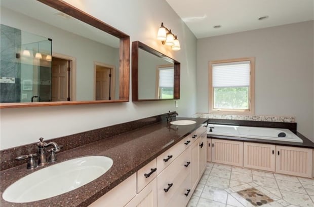 Spacious traditional bathroom with cherry-framed mirrors, cream cabinets, dark counters, and jet tub before remodel