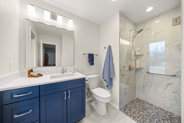 Modern hall bathroom with navy blue vanity, marble shower walls, pebble shower floor, and modern light bar