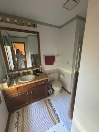 Dated hall bathroom with oak vanity, vanity strip lighting, and basic mirror before remodel