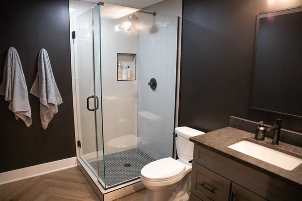 Dramatic dark hall bathroom with black walls, herringbone wood floor, white-tile shower, and modern fixtures