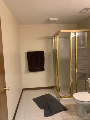 Outdated hall bathroom with brass-framed glass shower, beige tile, and dated finishes before remodel