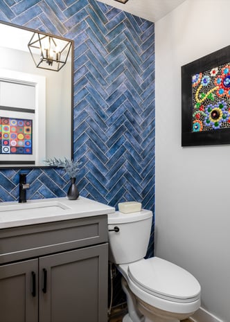 Modern powder room with blue herringbone feature wall, gray vanity, and black-framed mirror with cage pendant