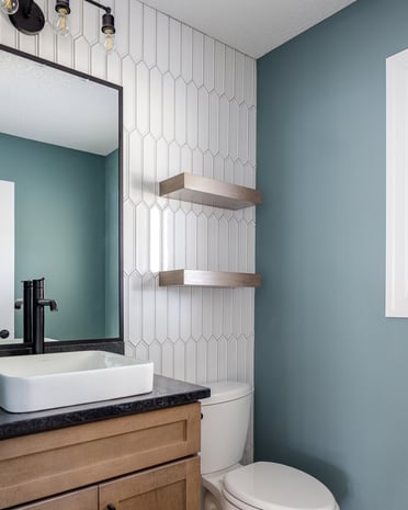 Modern powder room with teal walls, picket tile feature wall, floating oak vanity with vessel sink, and black mirror