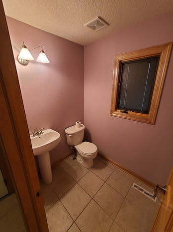 Tight powder room with mauve walls, oak trim, pedestal sink, and dated wall sconces before remodel