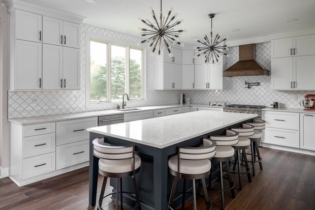 Modern white kitchen with arabesque tile backsplash, sputnik chandeliers, marble waterfall island, and navy base cabinets