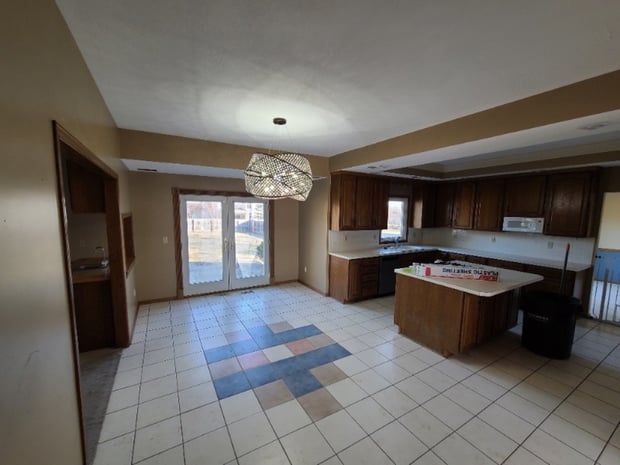 Empty pre-renovation kitchen with dark oak cabinets, multicolored vinyl floor tiles, and original hood before remodel
