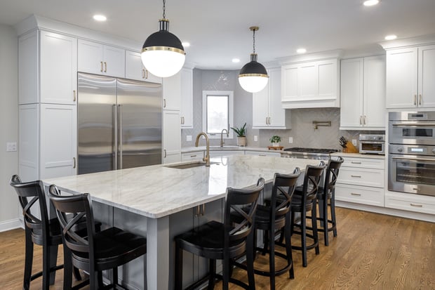 Bright transitional kitchen with white shaker cabinets, herringbone backsplash, marble waterfall island, and globe pendants