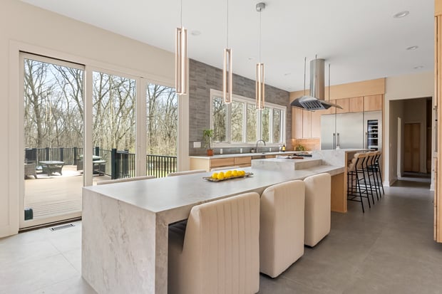 Open modern kitchen with light wood cabinets, marble waterfall island, and linear tube pendant lights