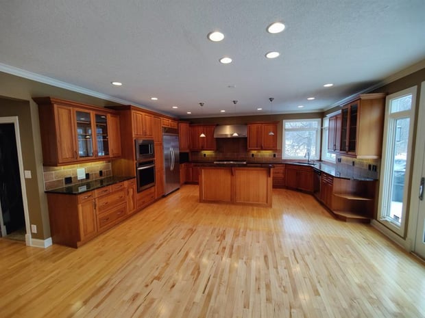 Empty pre-renovation kitchen with dark oak cabinets, dark green countertops, and dated vinyl floor tiles