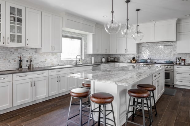 Bright white modern kitchen with marble island, glass globe pendants, and herringbone tile backsplash