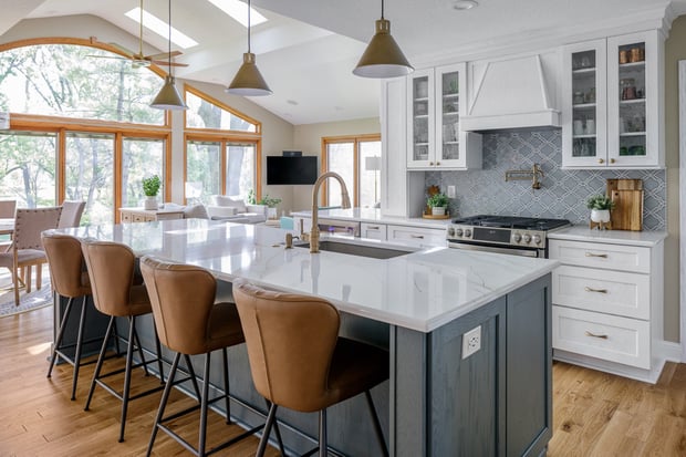 Modern kitchen with white cabinets, marble waterfall island, gray-blue base, and tan leather barstools