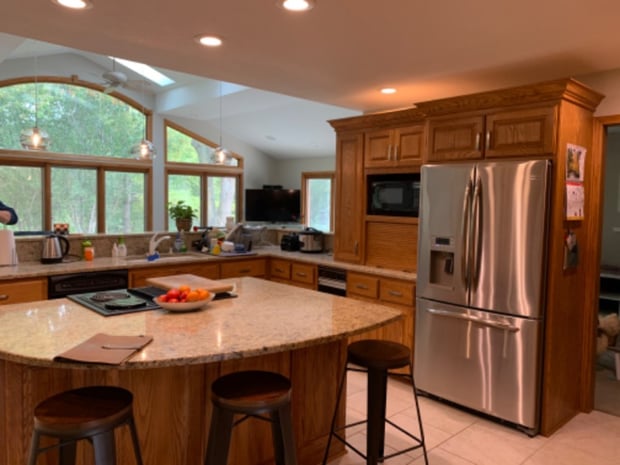 Traditional kitchen with oak cabinets, arched window wall, granite peninsula, and dated pendant lights before remodel