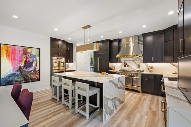 Sophisticated kitchen with espresso cabinets, brass-trimmed range hood, marble counters, and modern artwork