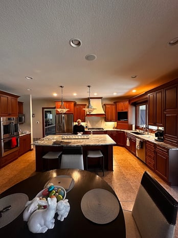 Traditional kitchen with dark cherry cabinets, granite island, large dome pendant lights, and tile floor before remodel