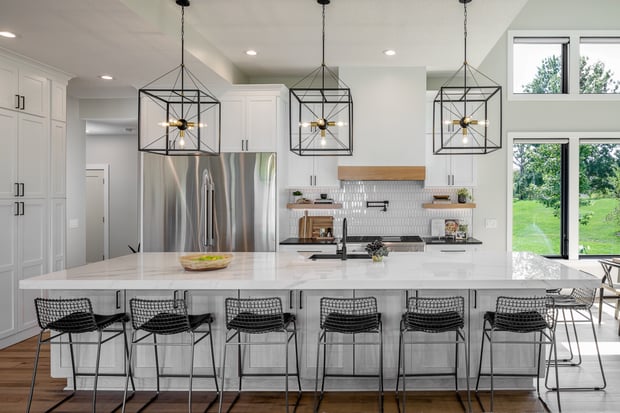 Bright white kitchen with marble counters, glass globe pendants, dark wood flooring, and leather-topped barstools