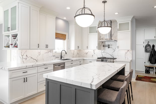Modern white kitchen with marble waterfall island, dome pendants, gray base, and adjacent mudroom