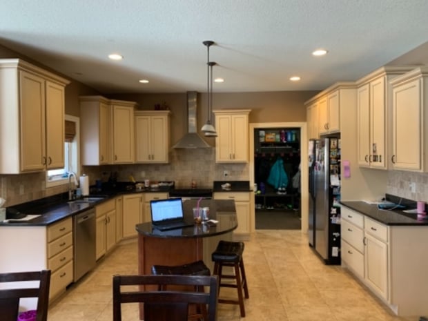 Cream traditional kitchen with stainless hood, brick backsplash, dark stone counters, and recessed pendants