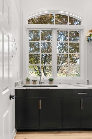 Modern utility room with arched window, marble counter, black cabinets, and brass fixtures
