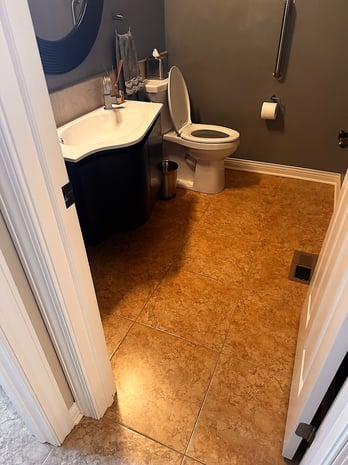 Outdated powder room with curved black vanity, faux-marble counter, brown walls, and tile floor before remodel