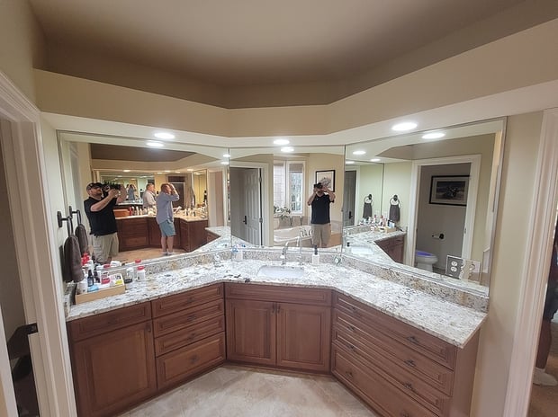 Traditional primary bathroom with corner vanity, wraparound mirrors, mocha cabinets, and granite counters before remodel