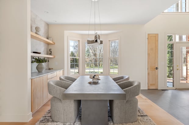 Modern dining room with sculptural metal pendant, upholstered chairs, light wood built-ins, and sage accent wall