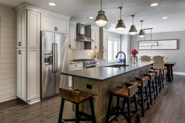 Modern open-concept kitchen with white shaker cabinets, dark counters, lantern pendants, and reclaimed-wood barstools