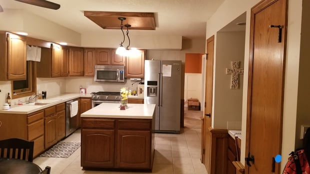 Traditional oak kitchen with white laminate counters, single pendant light, and beige tile floor before remodel